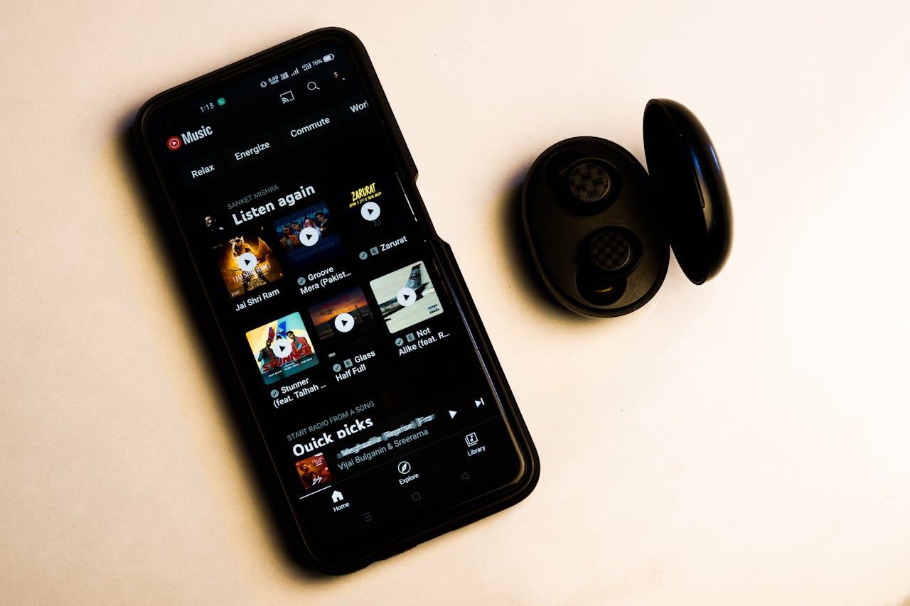 services-01 A smartphone displaying a music app interface with wireless earbuds on a plain background.