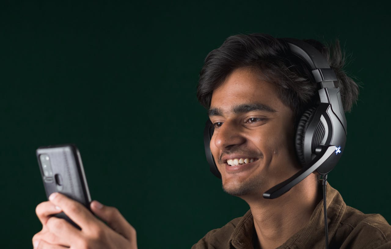 our-story Smiling young man using a smartphone with headphones, enjoying music indoors.