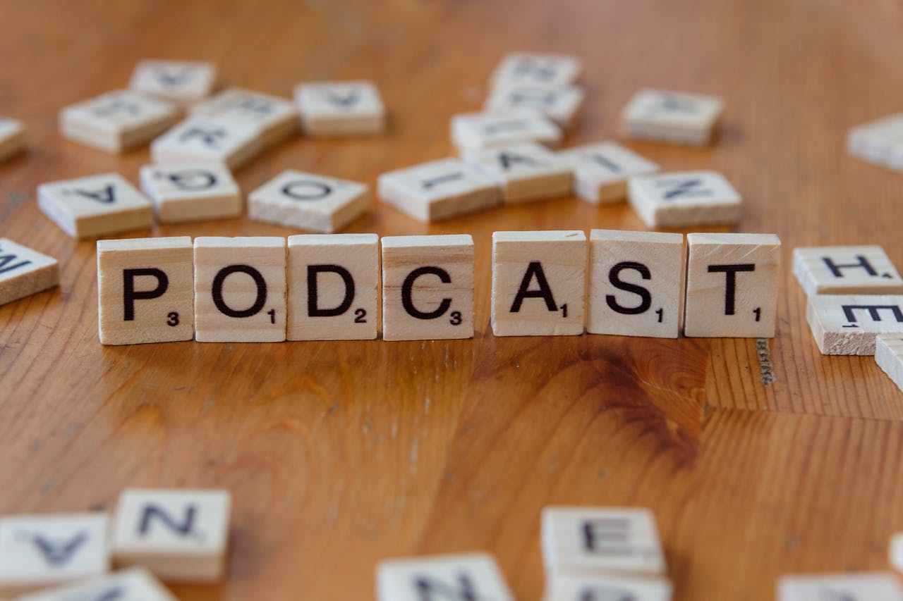 gallery-01 Scrabble tiles arranged to spell 'PODCAST' on a wooden surface with scattered letters.