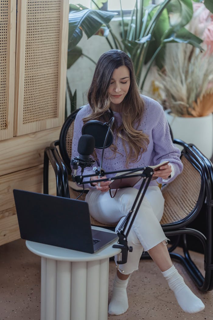 services-04 High angle full body if female host sitting in armchair with crossed legs and recording audio on laptop with microphone